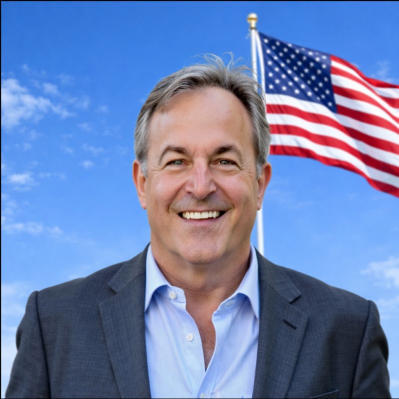 Chris Bezick smiling in a grey suit, an American flag flying behind him